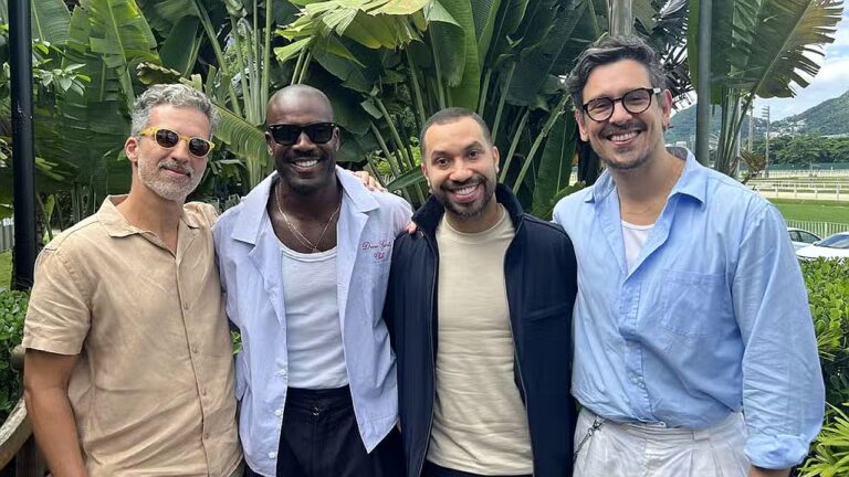 Quatro homens sorriem juntos ao ar livre diante de plantas tropicais em encontro informal