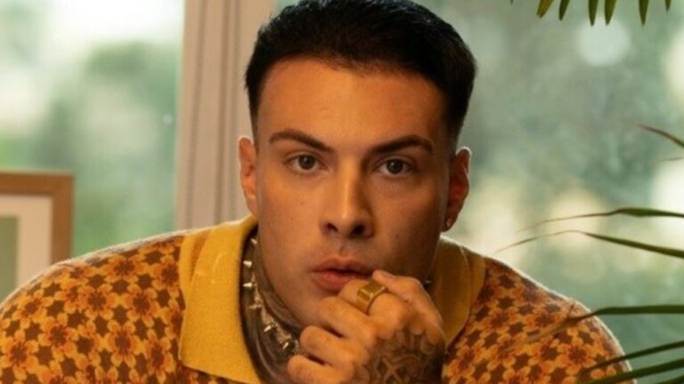 Rafa Marttinz olha surpreso com a mão na boca em ambiente interno com janela e plantas ao fundo