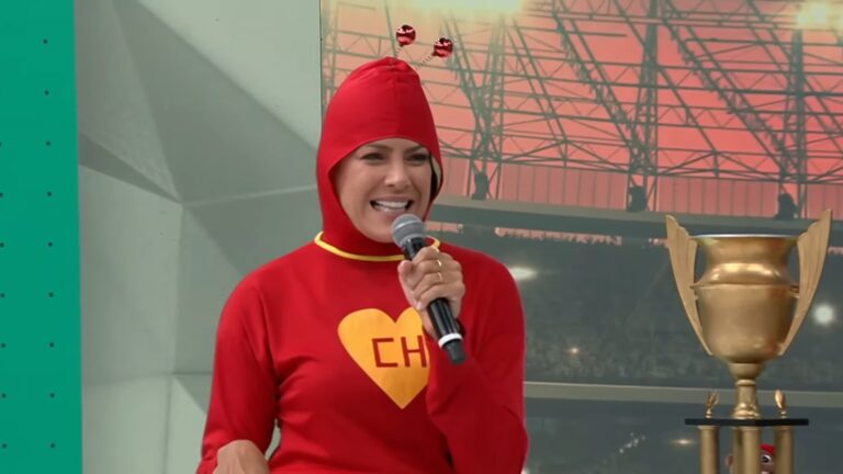 Renata Fan, vestida de Chapolin Colorado, fala ao microfone no palco do Jogo Aberto com troféu ao lado.