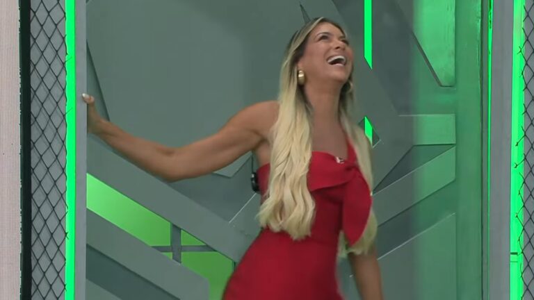 Renata Fan, de vestido vermelho, ri ao entrar no estúdio do Jogo Aberto, com iluminação verde e cenário moderno ao fundo.
