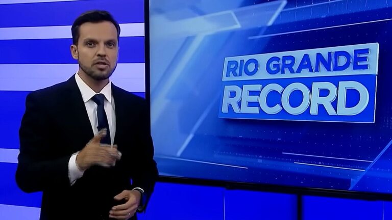 Apresentador fala ao vivo diante de telão com logotipo do jornal Rio Grande Record em estúdio de TV