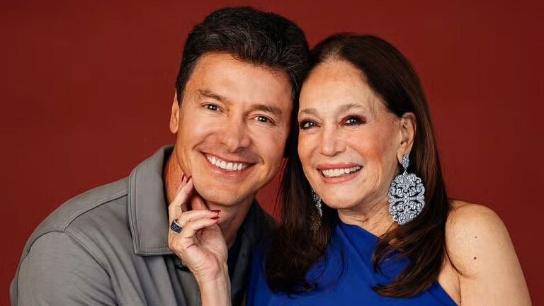 Homem e mulher sorriem juntos em retrato com fundo vermelho em foto promocional