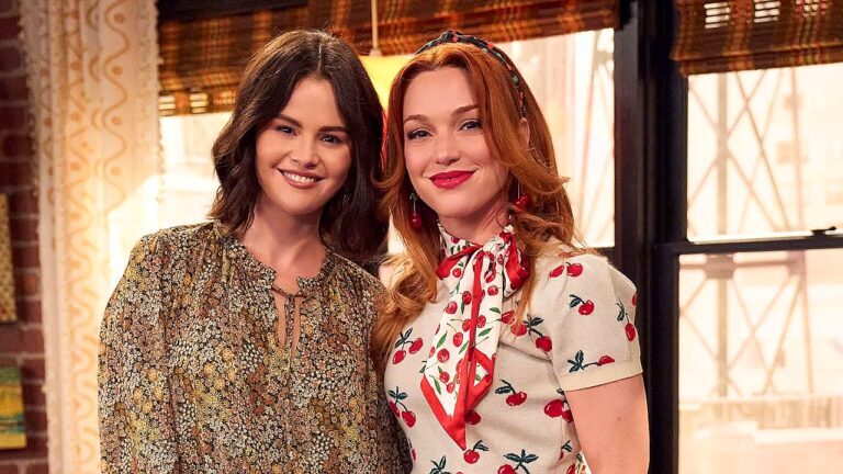 Selena Gomez e outra atriz posam sorrindo juntas em cena de série ambientada em apartamento com decoração retrô