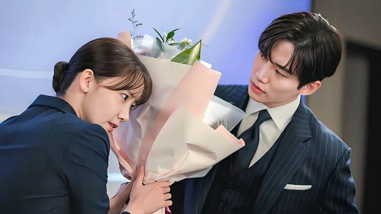 Homem de terno entrega buquê de flores a mulher surpresa em cena de drama coreano em ambiente corporativo