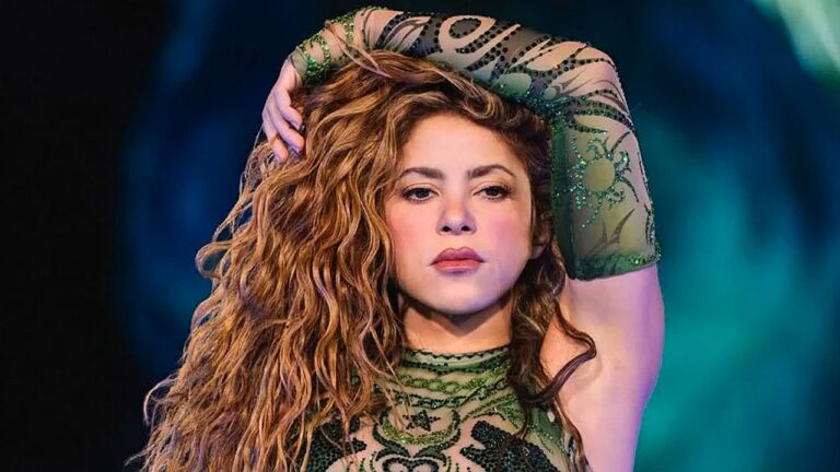 Cantora Shakira com cabelo cacheado posa com braço sobre a cabeça durante apresentação no palco