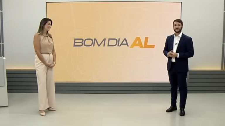 Thaíse Cavalcante e Ragi Torres apresentam o Bom Dia Alagoas em estúdio com telão ao fundo exibindo o nome do programa