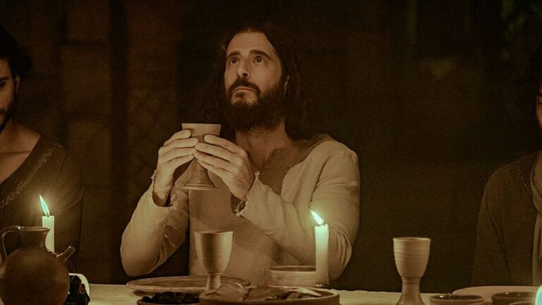 Homem caracterizado como Jesus segura cálice durante ceia à luz de velas em cena bíblica de série ou filme