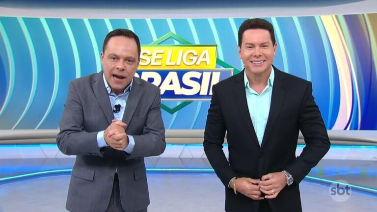 Thiago Gardinali e Marcão do Povo, apresentadores do SBT, sorriem no estúdio do Se Liga, Brasil diante de telão com logo do programa.
