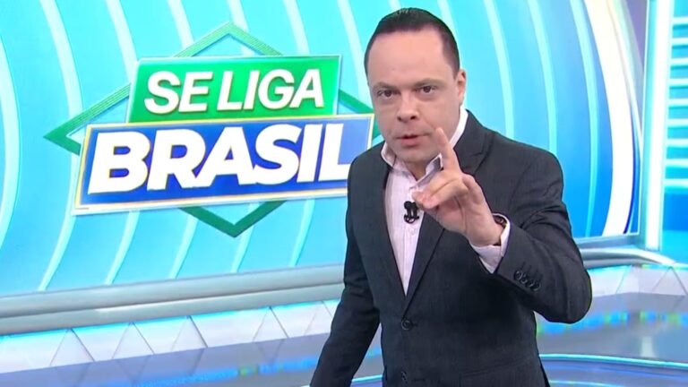 Apresentador Thiago Gardinali aponta para câmera durante o programa Se Liga, Brasil no estúdio do SBT.