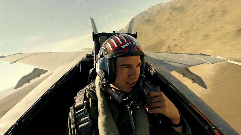 Piloto usa capacete dentro de caça militar durante voo sobre região desértica visto da cabine