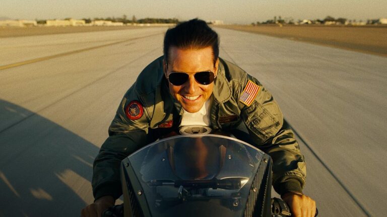 Piloto com óculos escuros em moto na pista de aeroporto em cena do filme Top Gun Maverick