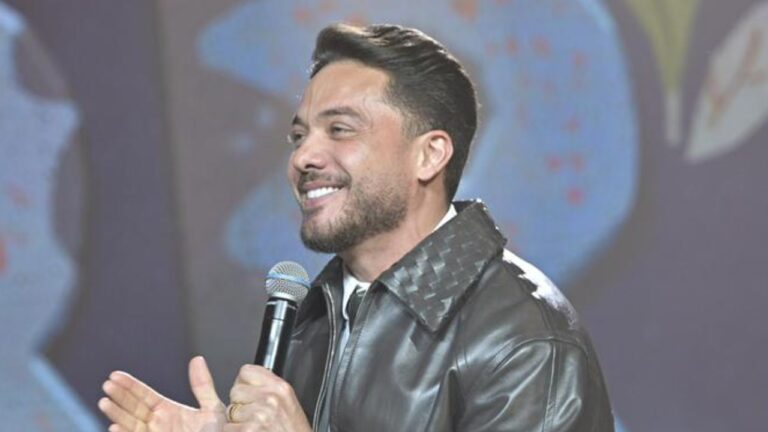 Wesley Safadão canta segurando microfone em palco com iluminação ao fundo durante apresentação musical