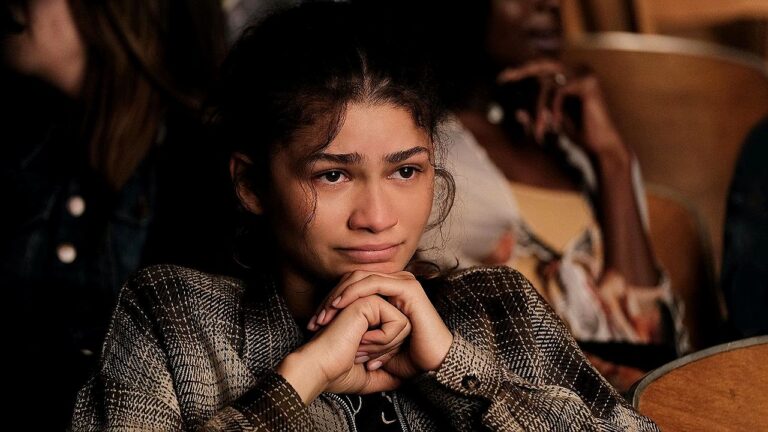 Mulher com expressão emocionada e olhos marejados apoia o queixo nas mãos em cena de série dramática