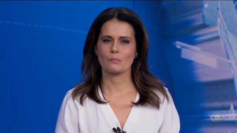 Adriana Araújo apresenta o Jornal da Band usando blusa branca em estúdio com fundo azul.