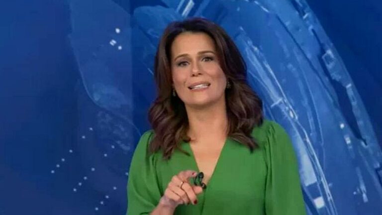 Mulher de vestido verde apresenta telejornal em estúdio com fundo azul e aponta para a câmera