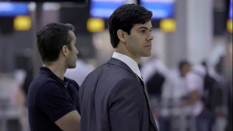 Homem de terno observa movimentação em aeroporto ao lado de outro homem