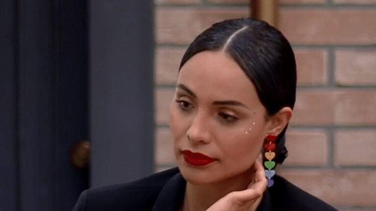 Mulher de batom vermelho e brincos coloridos participa de conversa em reality show