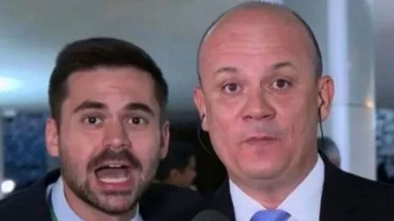 Dois repórteres aparecem em transmissão ao vivo falando para a câmera em ambiente interno com microfone e ponto eletrônico