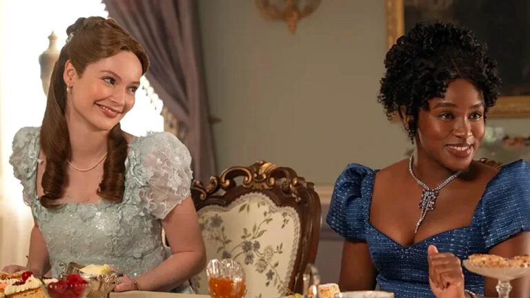 Duas mulheres com vestidos elegantes conversam durante jantar em cena da série Bridgerton