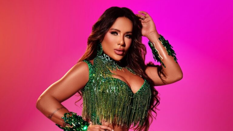 Carla Silva posa com figurino verde brilhante e franjas diante de fundo rosa em ensaio promocional