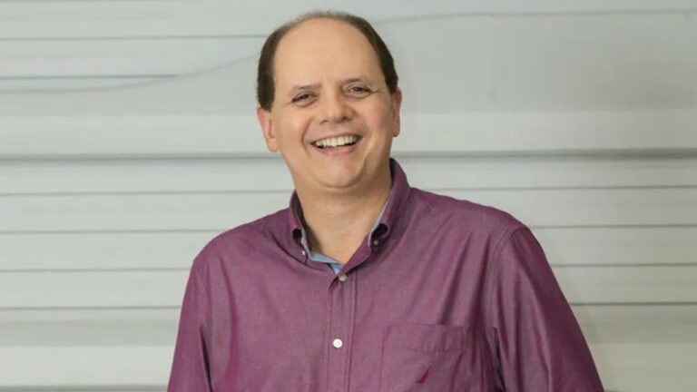 Carlos Jardim, executivo da GloboNews, sorri para foto com camisa vinho diante de parede clara em retrato usado em reportagem sobre televisão.