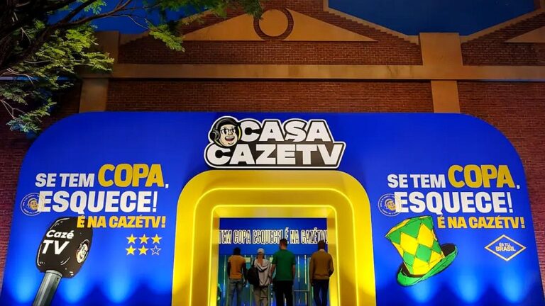 Fachada da Casa CazéTV com campanha da Copa exibida em estrutura iluminada durante evento esportivo