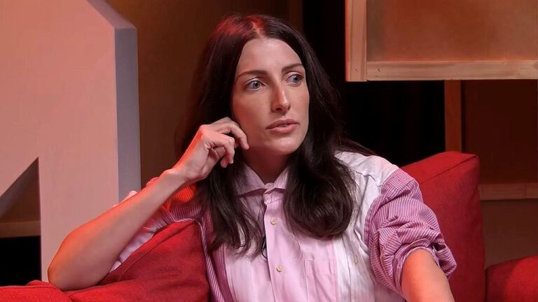 Mulher de camisa listrada participa de entrevista em programa com iluminação vermelha no estúdio