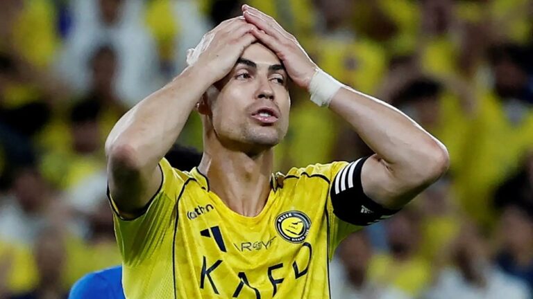 Cristiano Ronaldo, jogador do Al-Nassr, leva as mãos à cabeça durante partida de futebol com torcida ao fundo no estádio.