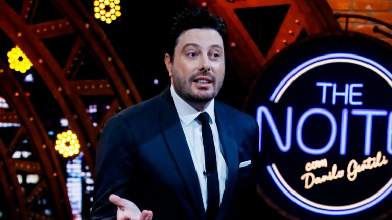 Danilo Gentili apresentando o The Noite diante do logotipo do programa iluminado no estúdio do SBT