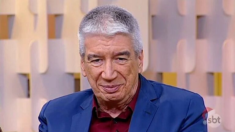 Apresentador de cabelo grisalho usa blazer azul durante programa do SBT no estúdio da emissora