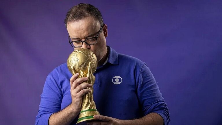 Homem com camisa da Globo segura e beija taça da Copa do Mundo diante de fundo roxo