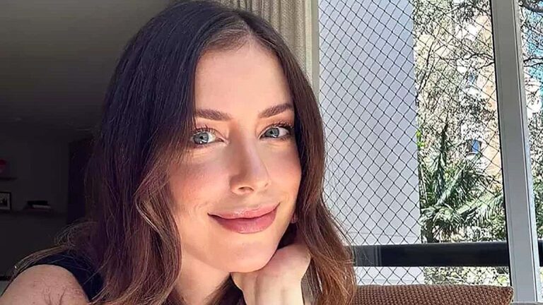 Mulher sorri em selfie tirada perto da janela de apartamento durante o dia