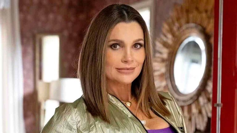 Atriz com jaqueta verde posa em ambiente interno com espelho ao fundo em cena de novela