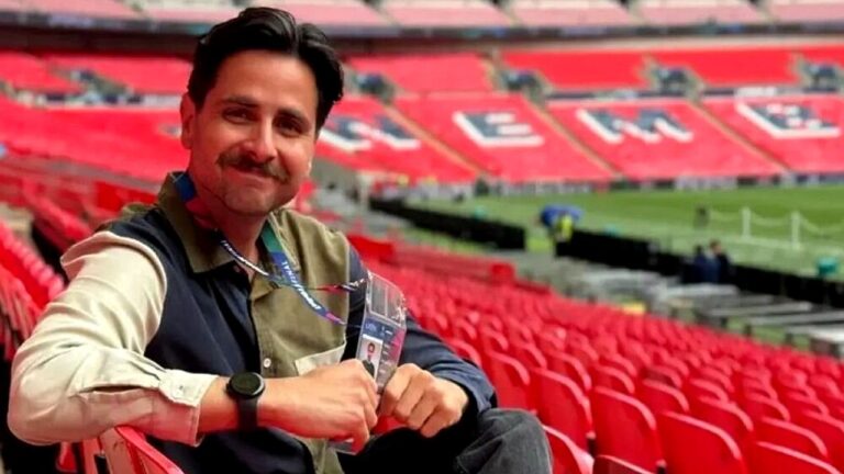 Homem sentado nas arquibancadas do estádio de Wembley durante cobertura esportiva de futebol