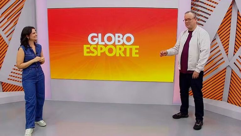 Apresentadores no estúdio do Globo Esporte diante de telão com logotipo do programa em fundo laranja