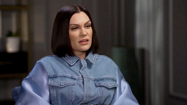 Cantora de cabelo preto participa de entrevista sentada em estúdio com roupa jeans clara