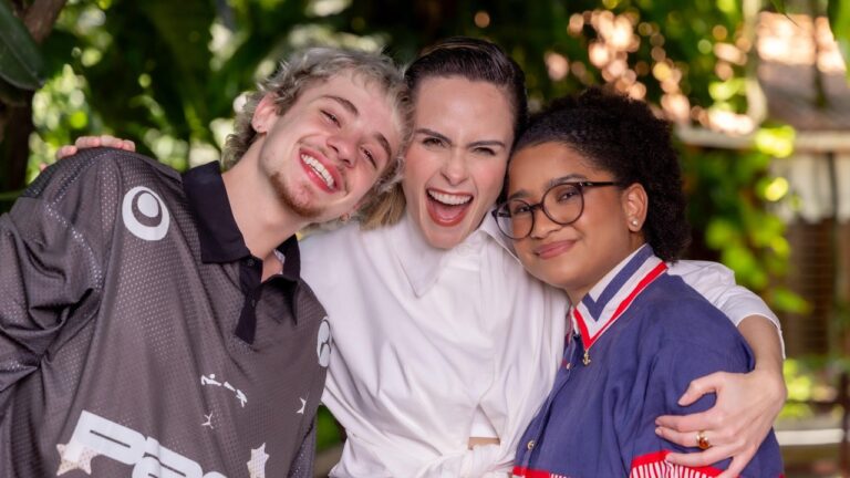 Juliano Floss, Ana Paula Renault e Milena abraçados e sorrindo juntos em área externa com vegetação ao fundo