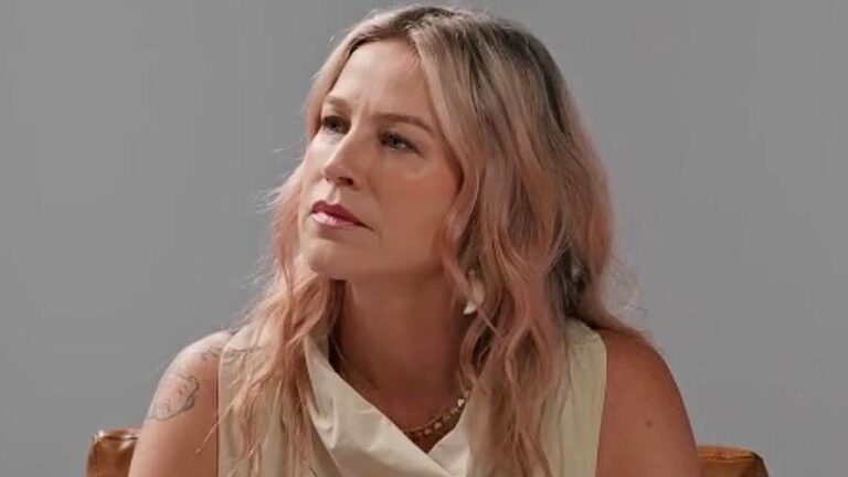 Mulher de cabelo rosa claro participa de entrevista em ambiente com fundo branco