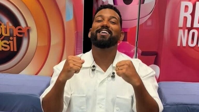 Homem de barba sorri e levanta os punhos durante programa de entretenimento em estúdio da Globo