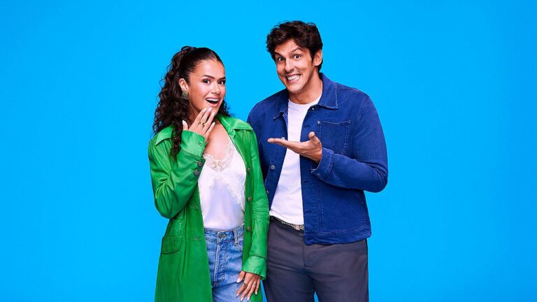 Homem aponta para mulher sorridente com mão no rosto em pose promocional sobre fundo azul sólido