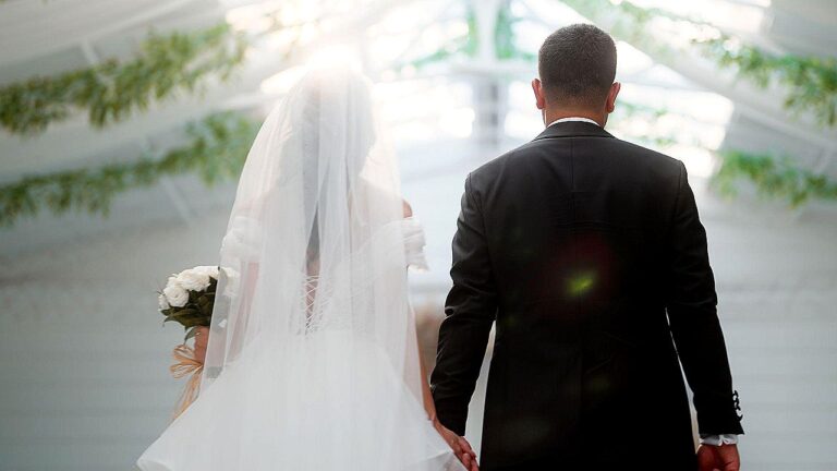 Noivos de mãos dadas caminham até o altar durante cerimônia de casamento em ambiente iluminado