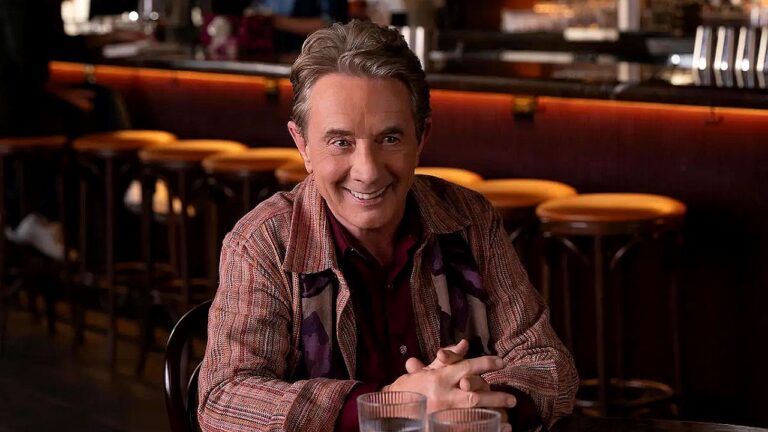 Personagem de Martin Short sorrindo em mesa de restaurante na série Only Murders in the Building