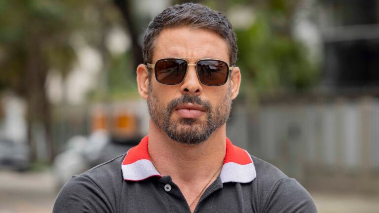 Cauã Reymond como Mauricio usa óculos escuros e encara a câmera em cena da série Jogada de Risco