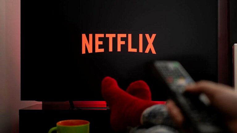 Logotipo da Netflix exibido na televisão enquanto pessoa segura controle remoto na sala escura