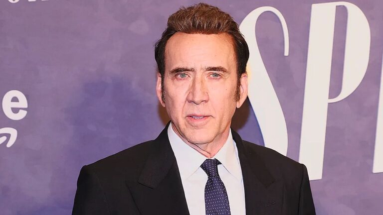 Nicolas Cage posa de terno e gravata durante evento com painel roxo ao fundo