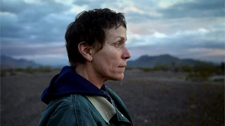 Mulher observa horizonte em paisagem desértica com expressão séria em cena de filme dramático