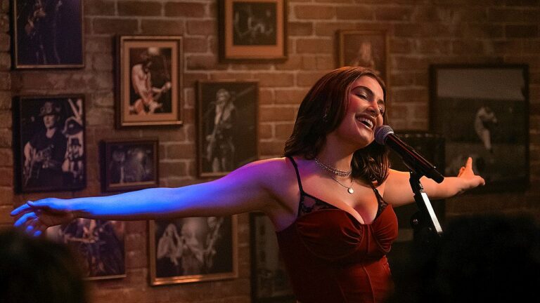 Cantora de vestido vermelho se apresenta com braços abertos em bar com fotos musicais na parede
