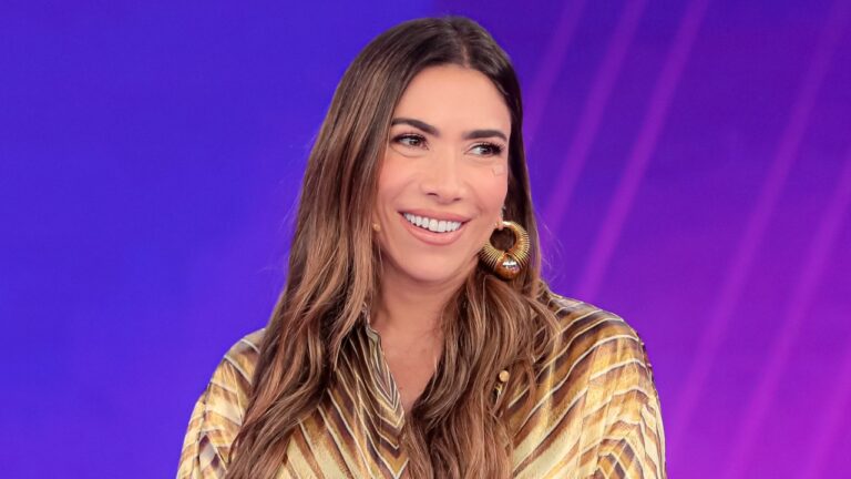 Patricia Abravanel sorri no palco do Programa Silvio Santos com fundo iluminado em tons de roxo