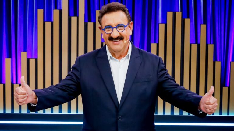Ratinho sorri e faz sinal de positivo com os polegares durante gravação de programa em estúdio iluminado do SBT