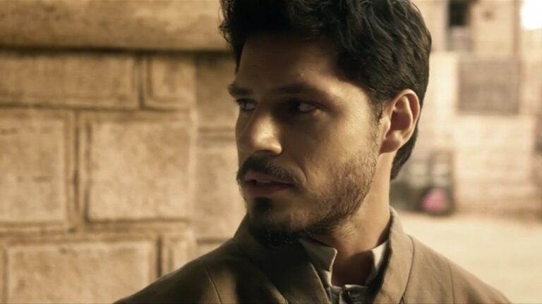 Homem de barba olha para o lado em cena da novela Reis, da Record, ambientada em rua antiga.